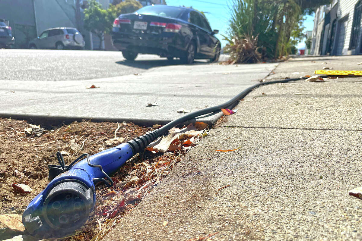 A charging cord for electric vehicles is seen strung across a public sidewalk. The great transition to electric vehicles is under way for homeowners who can charge their cars in a private garage, but for millions of renters access to charging remains a significant barrier.