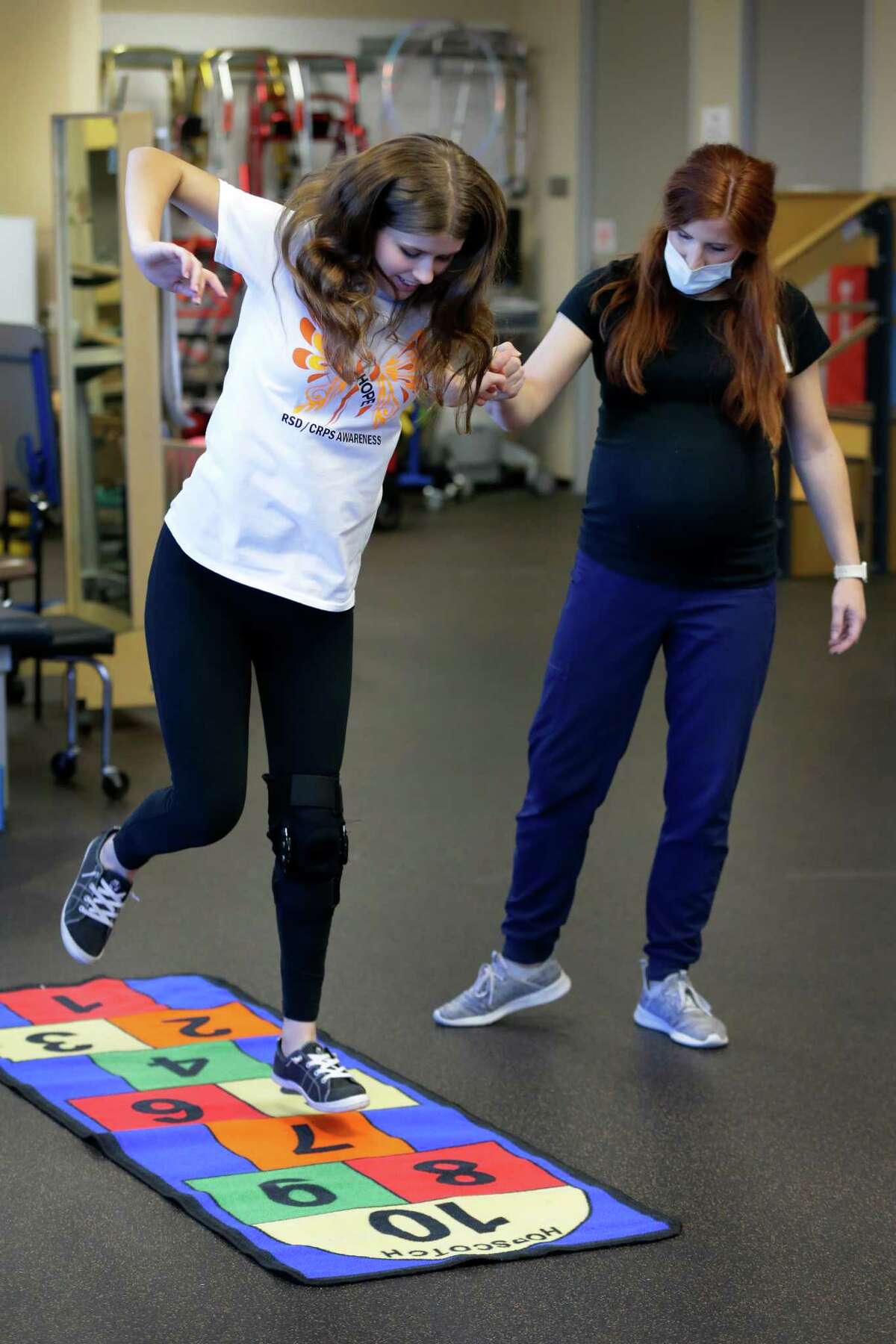 Kaitlin Thibodeaux, left, a 14 year old with chronic regional pain syndrome in her left ankle, gets some assistance as she jumps hop-scotch as she goes thru her physical therapy session with Katelyn Navarro, right, at TIRR Memorial Hermann Wednesday, Oct. 26, 2022 in The Woodlands, TX.