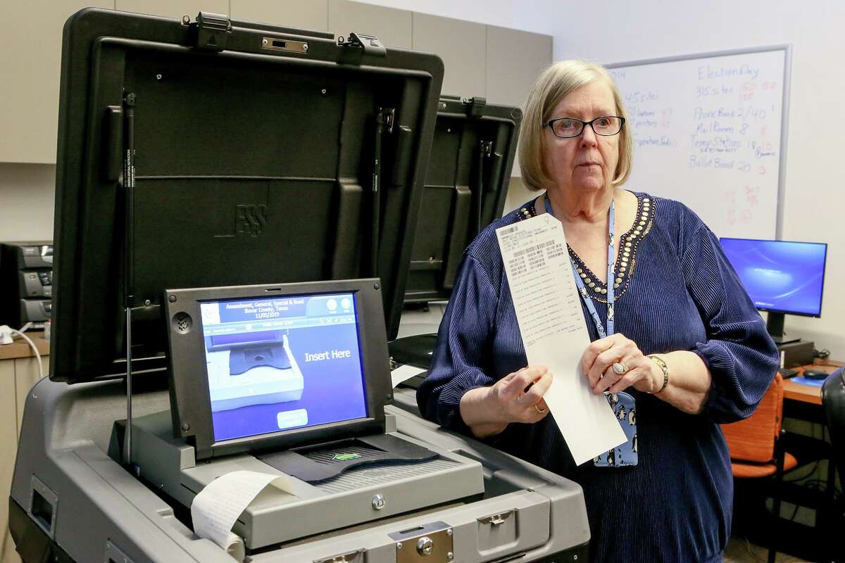 Bexar County Elections Administrator Jacque Callanen holds a sample paper ballot like those that are inserted into the ballot scanners and vote tabulators, left, to record votes.