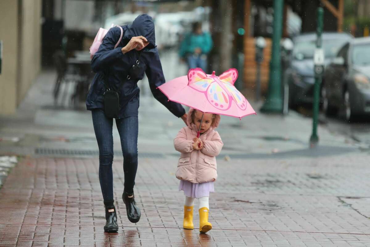 A woman and child cross Park Street during a steady rainfall in Alameda, Calif., on Nov. 1, 2022.