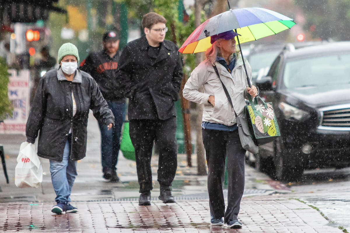 People cross a street during a rain storm in Alameda on Nov 1, 2022.