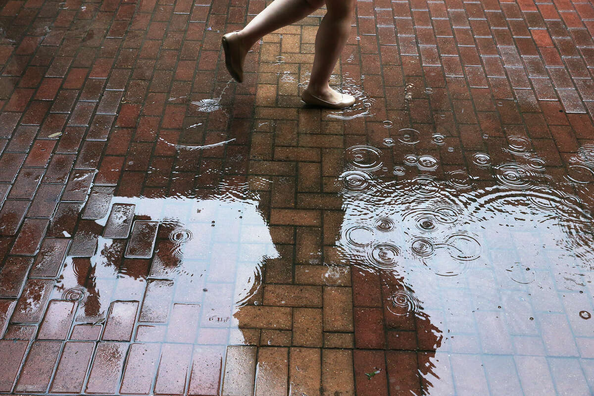 A pedestrian tries to avoid puddles while walking along East Houston Street in downtown San Antonio on Monday, May 6, 2019. The National Weather Service is predicting damaging winds and hail Friday night. 