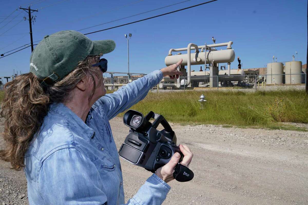 Sharon Wilson, holding a thermal imaging camera, points to tanks she said were leaking methane in Arlington, Texas, Tuesday, Oct. 18, 2022. Wilson, a field advocate for Earthworks, which promotes alternatives to fossil fuels, uses the camera to detect methane leaks at oil and gas facilities.