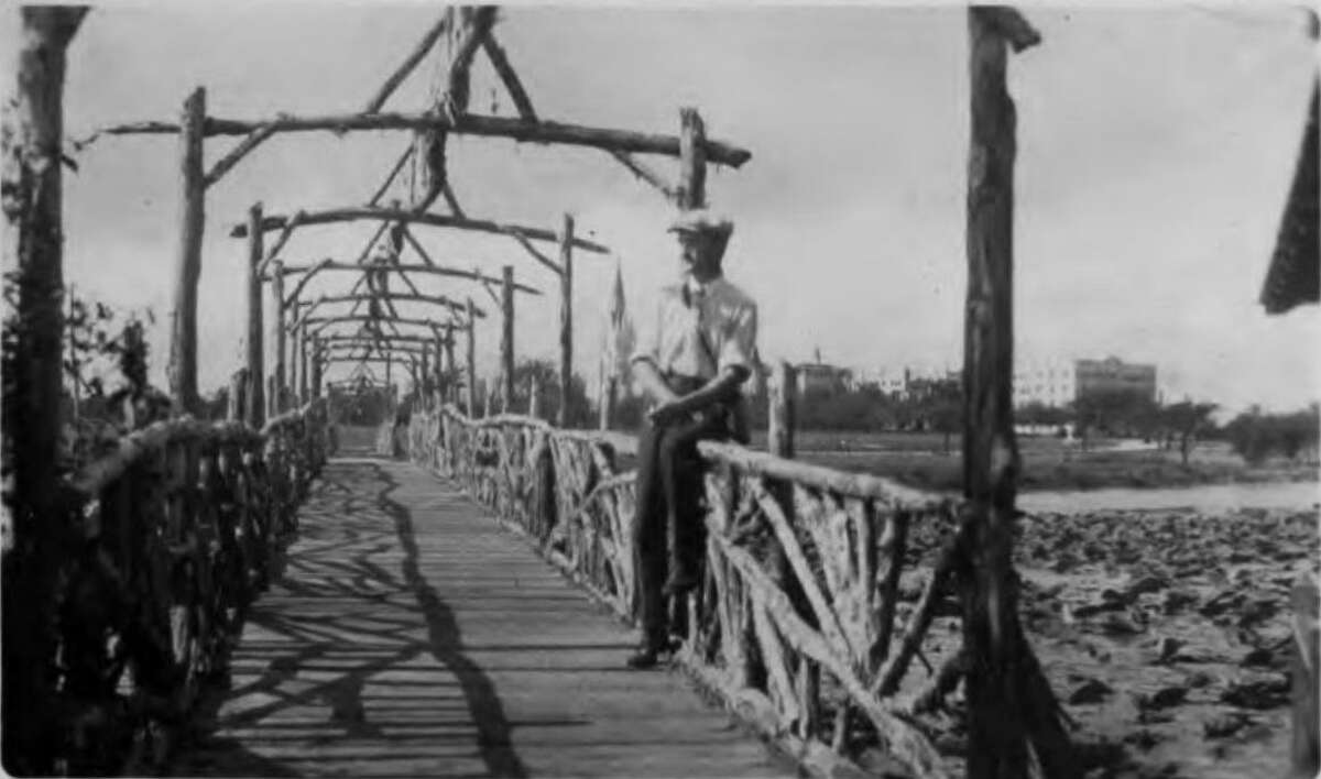 Photographer Al Schaal poses circa 1927 on a pedestrian bridge at Elmendorf Lake, with Our Lady of the Lake College (now University) in the distance. The lake was a primary attraction of Lake View Gardens No. 1, a subdivision built nearby.