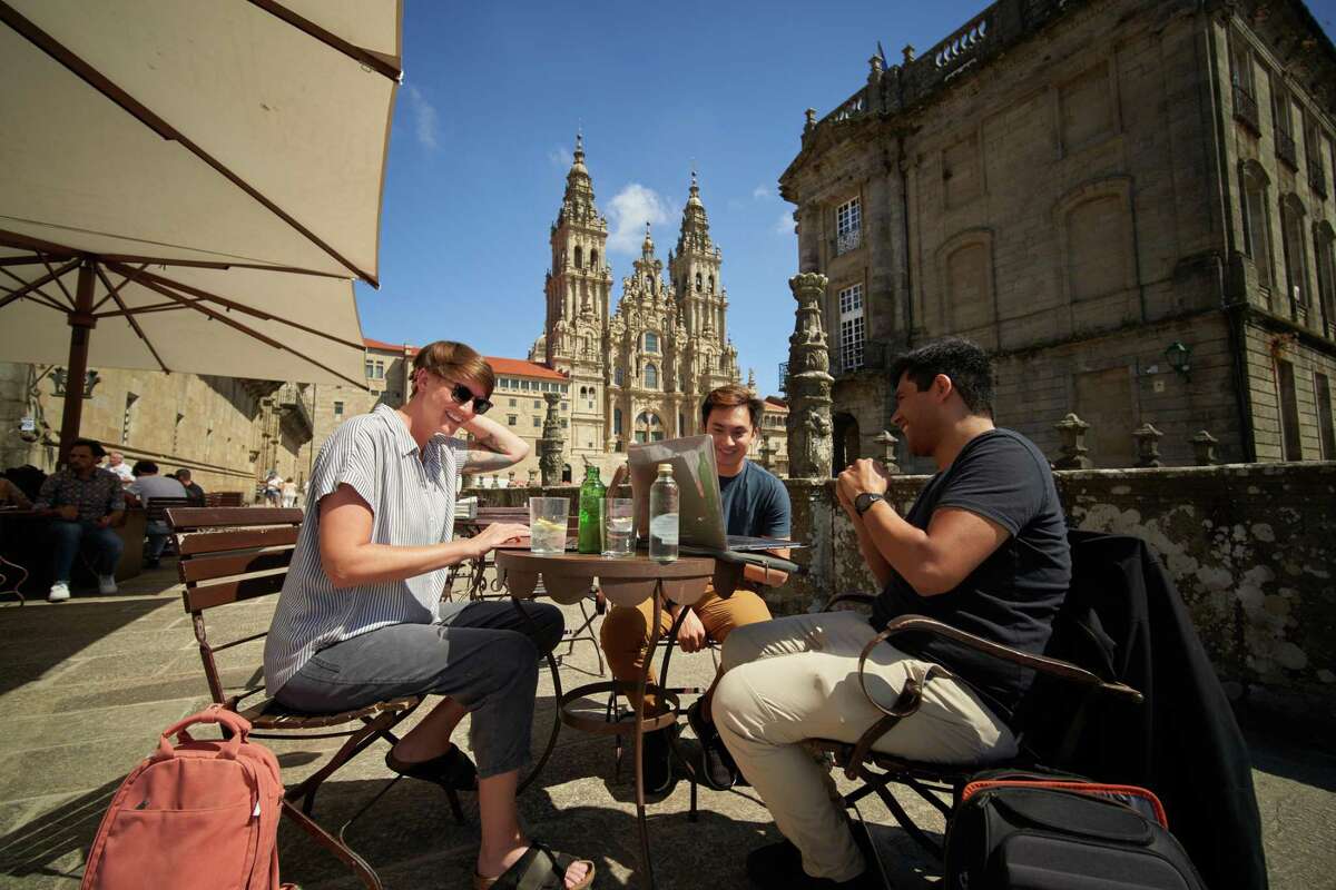 Expensify的员工Lauren Schurr, Jack Nam和Marco Chávez聚集在西班牙圣地亚哥德孔波斯特拉的Parador酒店外，以历史悠久的大教堂为背景。