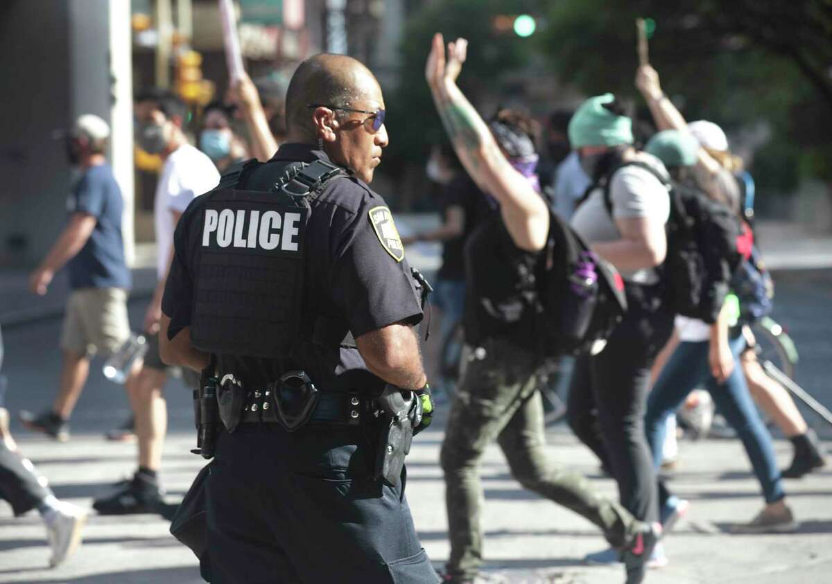 Protestors march downtown past a San Antonio Police officer to San Antonio Travis Park, on Wednesday, June, 3, 2020.
