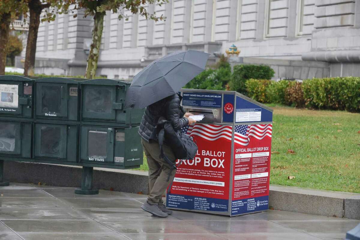 Ritchie Iu of San Francisco holds an umbrella as he places his ballot into an official ballot dropbox outside of City Hall on on Tuesday, November 8, 2022 in San Francisco, Calif.