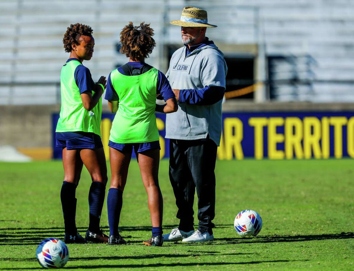 University of California Berkeley forwards Amaya Gray (11), left, and Anysa Gray (17), center, both 20, converse with head coach Neil McGuire during soccer practice at Edwards Stadium on Wednesday, October 26, 2022, in Berkeley, Calif. The twins, of East Palo Alto, faced homelessness during their childhood and worked through their first two years as student athletes.