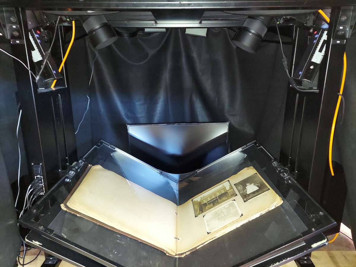 A photograph album is displayed at the Madison County Historical Archival Library on a book scanner, which uses two cameras for digitization. The MCHS also has a portable photo studio light box for photographing small and medium-sized objects.