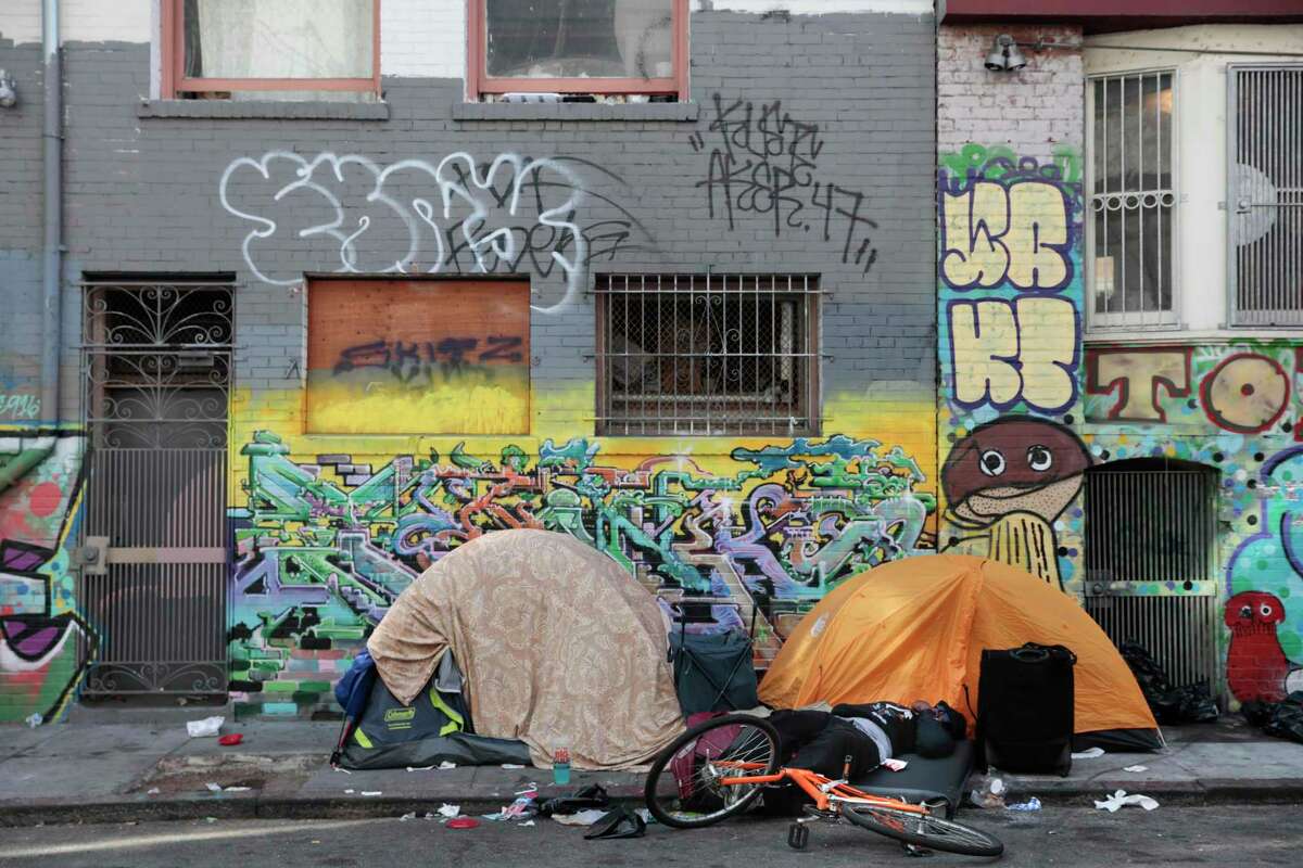 A man lies on a pad next to two tents on Hemlock Alley in San Francisco.