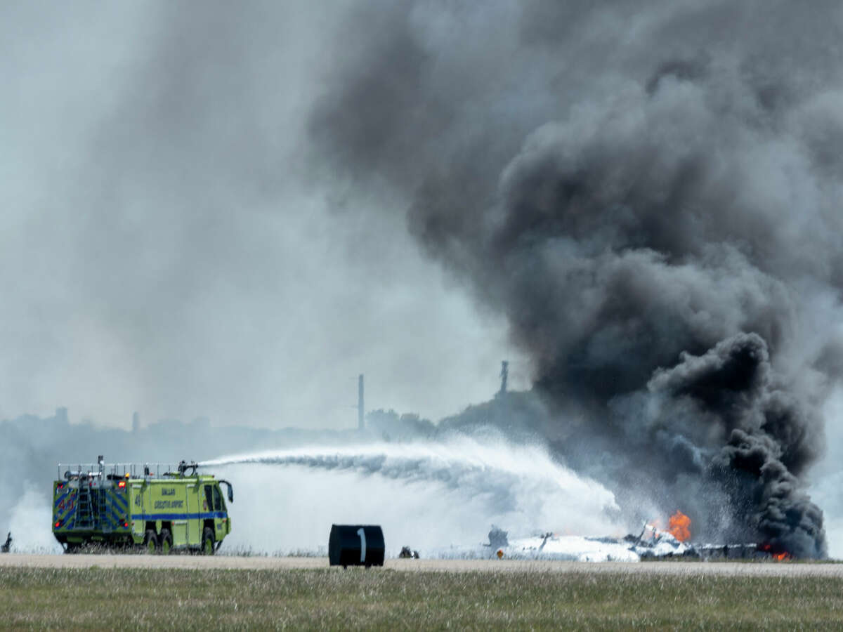 In this photo provided by Larry Petterborg, firefighters work at the crash scene after a Boeing B-17 Flying Fortress and a Bell P-63 Kingcobra collided in the midair during an airshow at Dallas Executive Airport in Dallas on Nov. 12, 2022. (Larry Petterborg via AP)