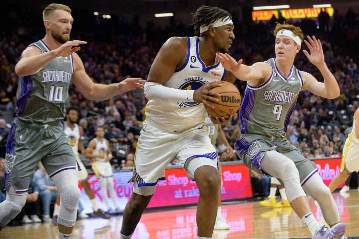 Golden State Warriors center Kevon Looney, center, is guarded by Sacramento Kings forward Domantas Sabonis (10) and guard Kevin Huerter (9) during the first quarter of an NBA basketball game in Sacramento, Calif., Sunday, Nov. 13, 2022. (AP Photo/Randall Benton)