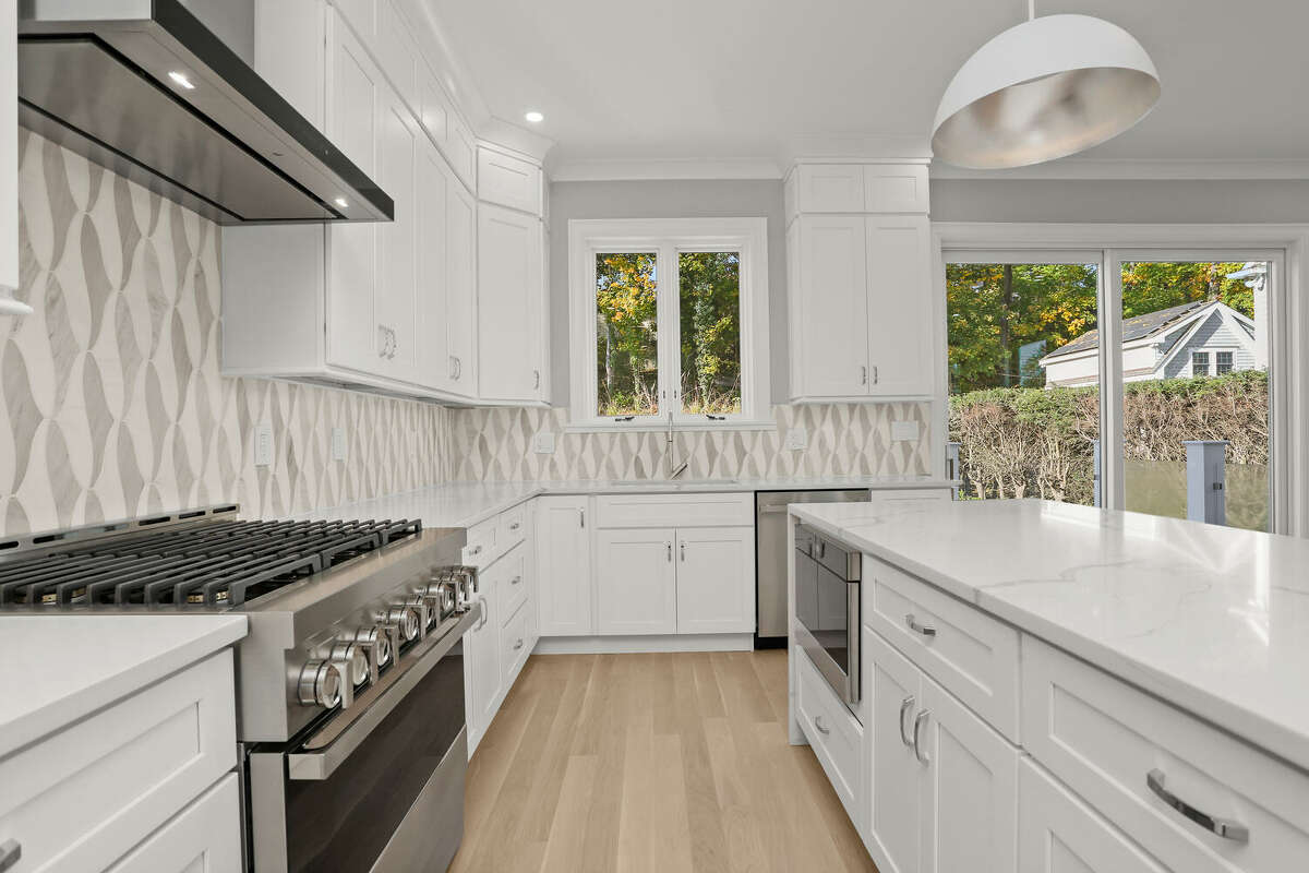 The kitchen is a bright and timeless space, with white cabinets, quartz counters, Jenn-Air NOIR appliances and a striking backsplash made of Manhattan Marble. 