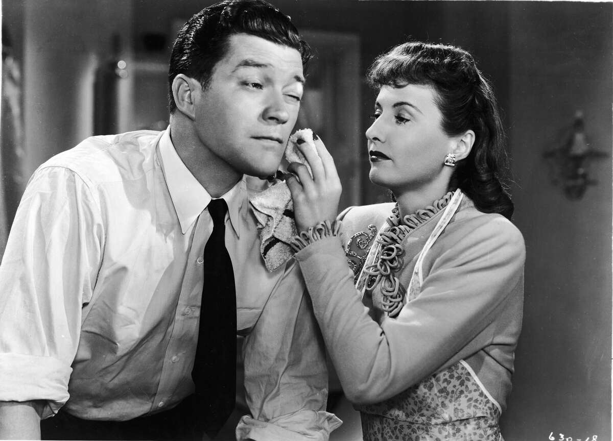 American actor Barbara Stanwyck (1907 - 1990) uses a washcloth to dab Dennis Morgan's face in a still from the film, 'Christmas in Connecticut,' directed by Peter Godfrey, 1945. (Photo by Warner Bros./Courtesy of Getty Images)