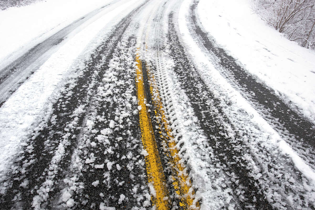 Tire treads are pressed into snow along an asphalt road