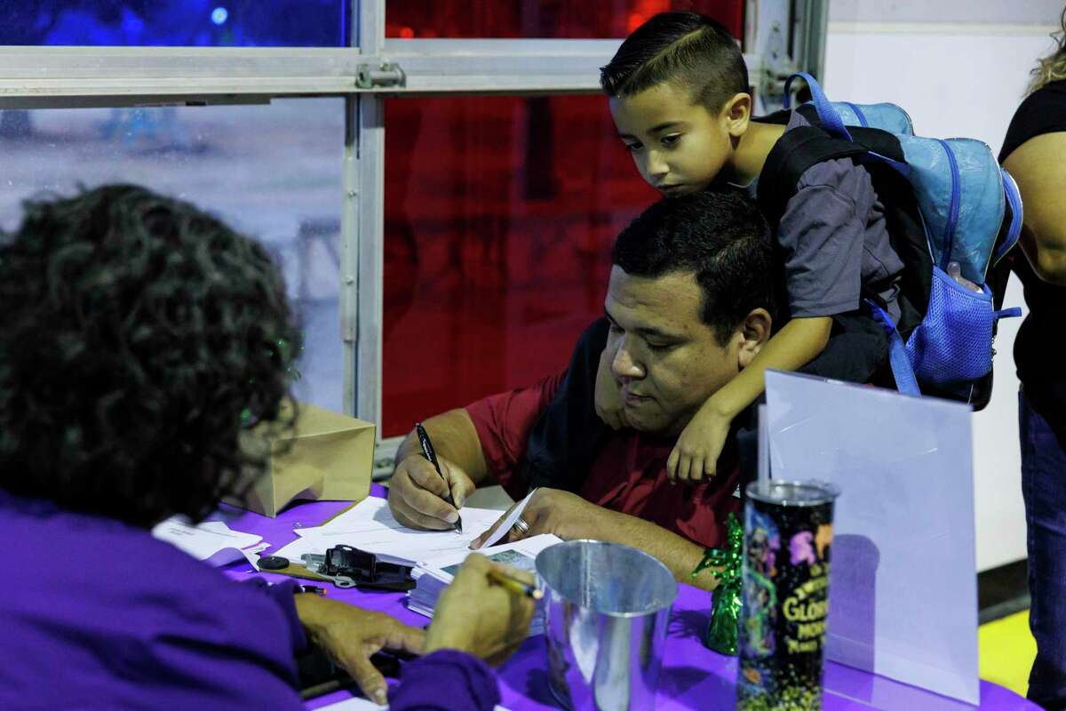 Michael Regino signs in for his Compadre y Compadre program graduation ceremony as his 5-year-old son Alex sits on his shoulders at The Children’s Shelter in San Antonio on Thursday. Regino’s wife, mother and two sons attended the commencement ceremony to celebrate him making it through the 15-week program.