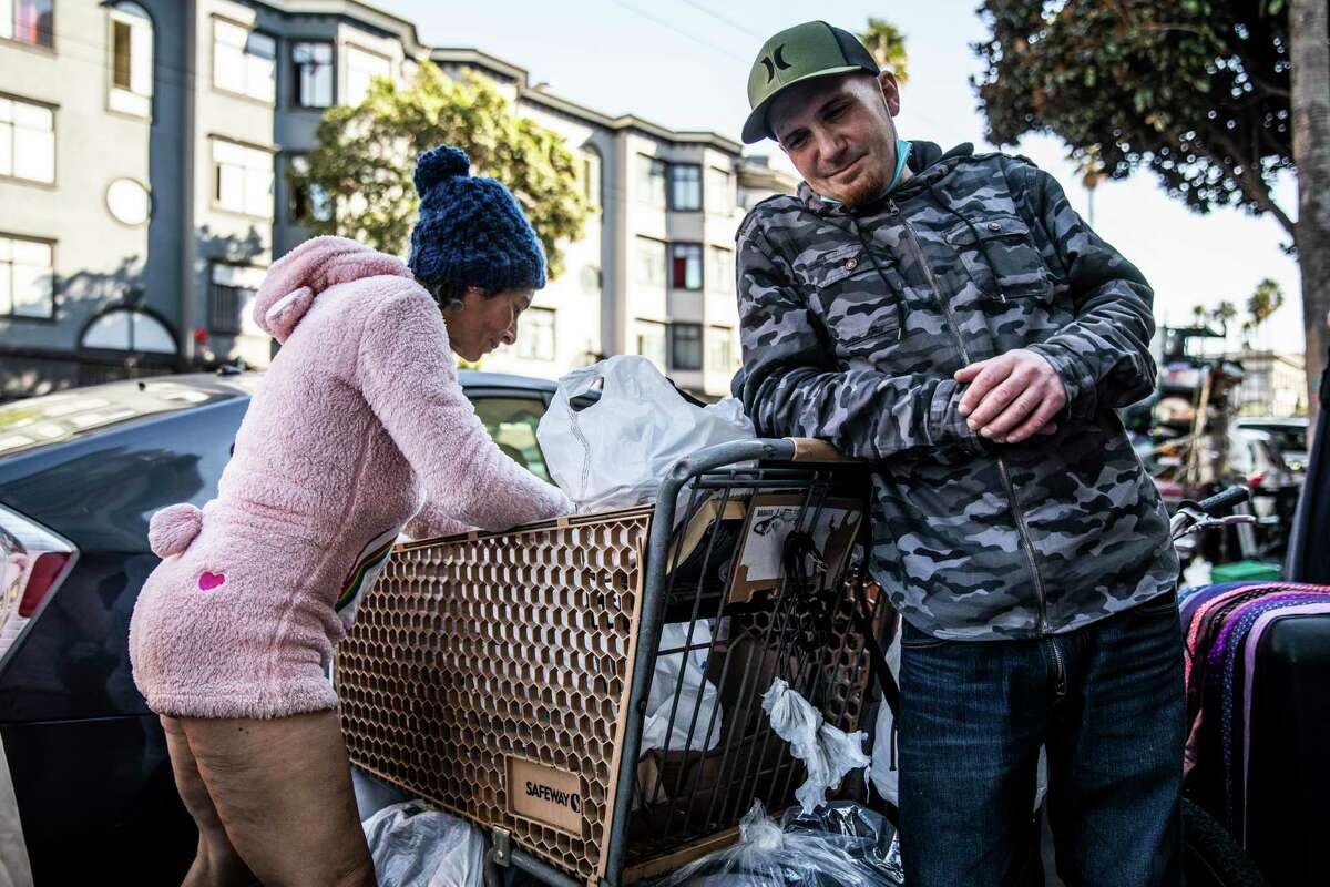 TJ Johnson, an unhoused San Francisco native who recently received housing through the city’s Tenderloin Center, smiles as girlfriend Justine works to sell merchandise at 16th and Mission streets. Johnson says he is a frequent visitor to the center because of fentanyl addiction.