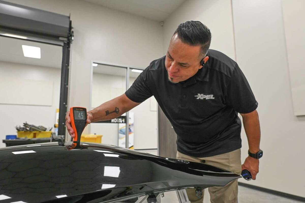 Rudy Robles checks the conditions for applying XPEL Inc.’s protective coating on a car hood at the company’s San Antonio headquarters.