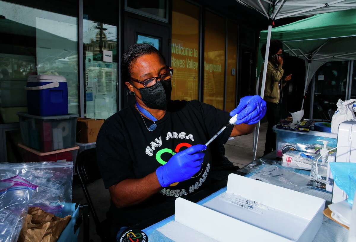 在加利福尼亚州旧金山海耶斯谷游乐场举行的社区卫生博览会上，金·罗兹医生(左)将新冠病毒加强疫苗放入针头中。