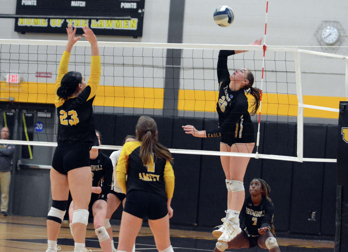 Trumbull's Camdyn Roth (26) sends the ball over the net. Vivian Cain (23) and Sabrina McGovern (4) of Amity defend in Wednesday's CIAC Class LL semifinal.