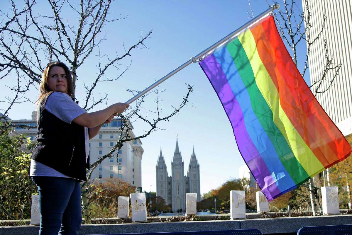 In this Nov. 14, 2015 file photo, Sandy Newcomb poses for a photograph with a rainbow flag as people gather for a mass resignation from The Church of Jesus Christ of Latter-day Saints in Salt Lake City. The Church of Jesus Christ of Latter-day Saints is repealing rules unveiled in 2015 that banned baptisms for children of gay parents and made gay marriage a sin worthy of expulsion. The surprise announcement Thursday, April 4, 2019, by the faith widely known as the Mormon church reverses rules that triggered widespread condemations from LGBTQ members and their allies. 