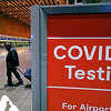 FILE - Travelers pass a sign near a COVID-19 testing site in Terminal E at Logan Airport, on Dec. 21, 2021, in Boston. (AP Photo/Charles Krupa, File)
