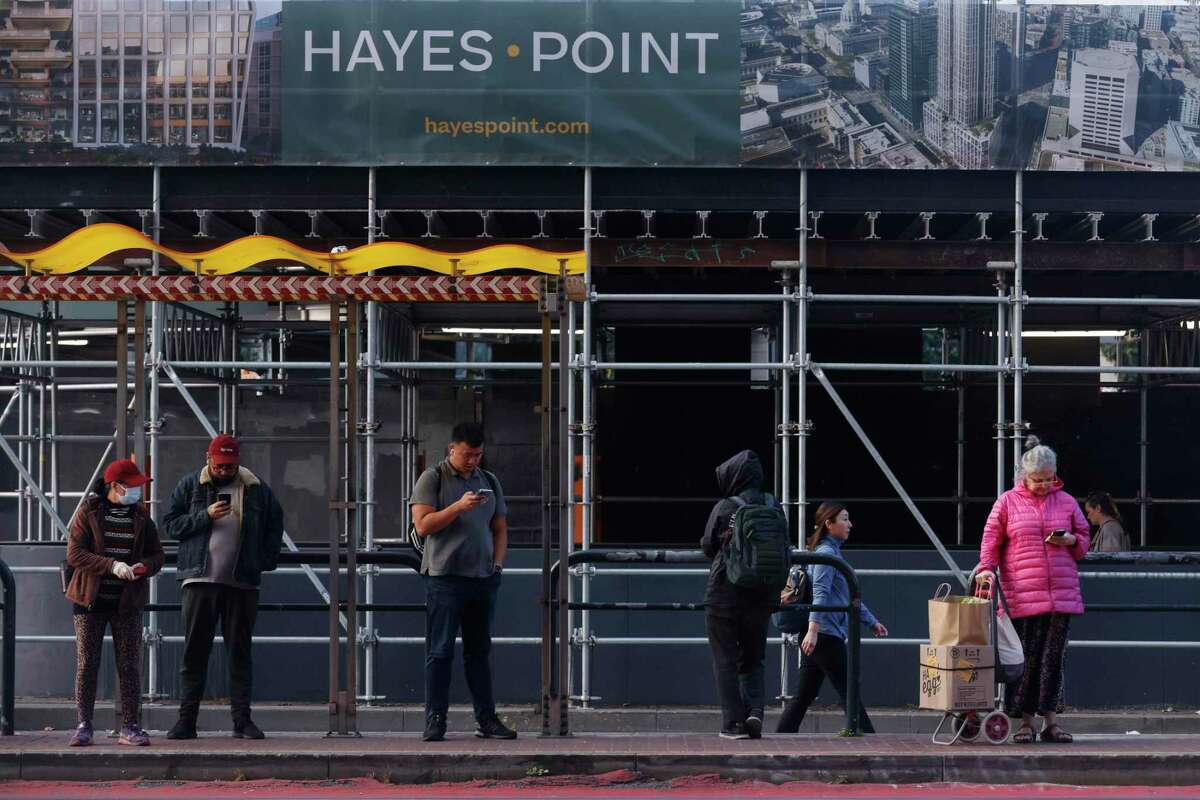 People at a Muni Stop stand in front of Hayes Point signage in San Francisco.