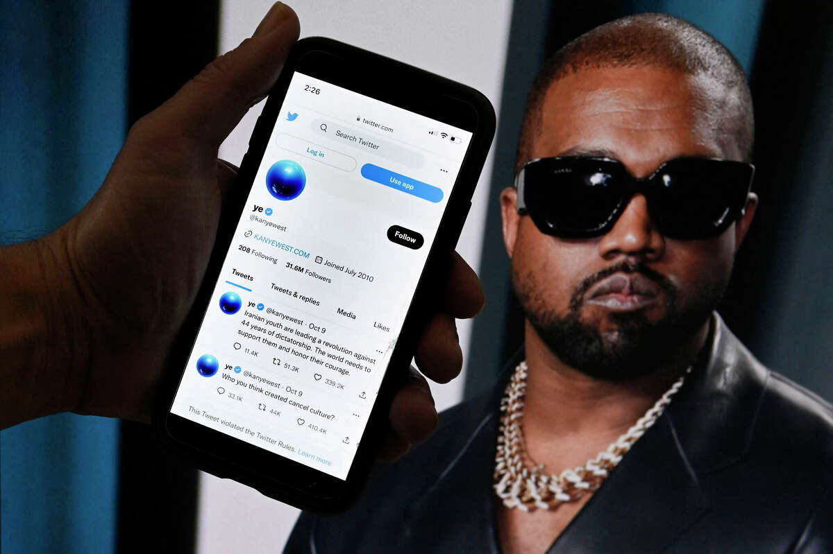 In this photo illustration, the Twitter account of Kanye West is displayed on a mobile phone with a photo of him shown in the background on October 28, 2022 in Washington, DC. - Rapper Kanye West's Twitter account, which was temporarily locked out after posting anti-Semitic remarks, appeared to be back up on the platform, on October 28 after billionaire Elon Musk took ownership of the social media company. (Photo by OLIVIER DOULIERY / AFP) (Photo by OLIVIER DOULIERY/AFP via Getty Images)