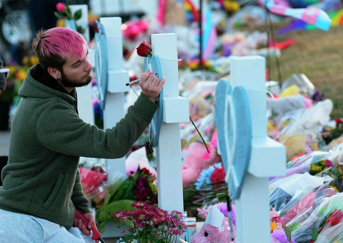 A man signs a cross at a makeshift tribute with a display of bouquets of flowers on a corner near the site of a mass shooting at a gay bar Monday, Nov. 21, 2022, in Colorado Springs, Colo.