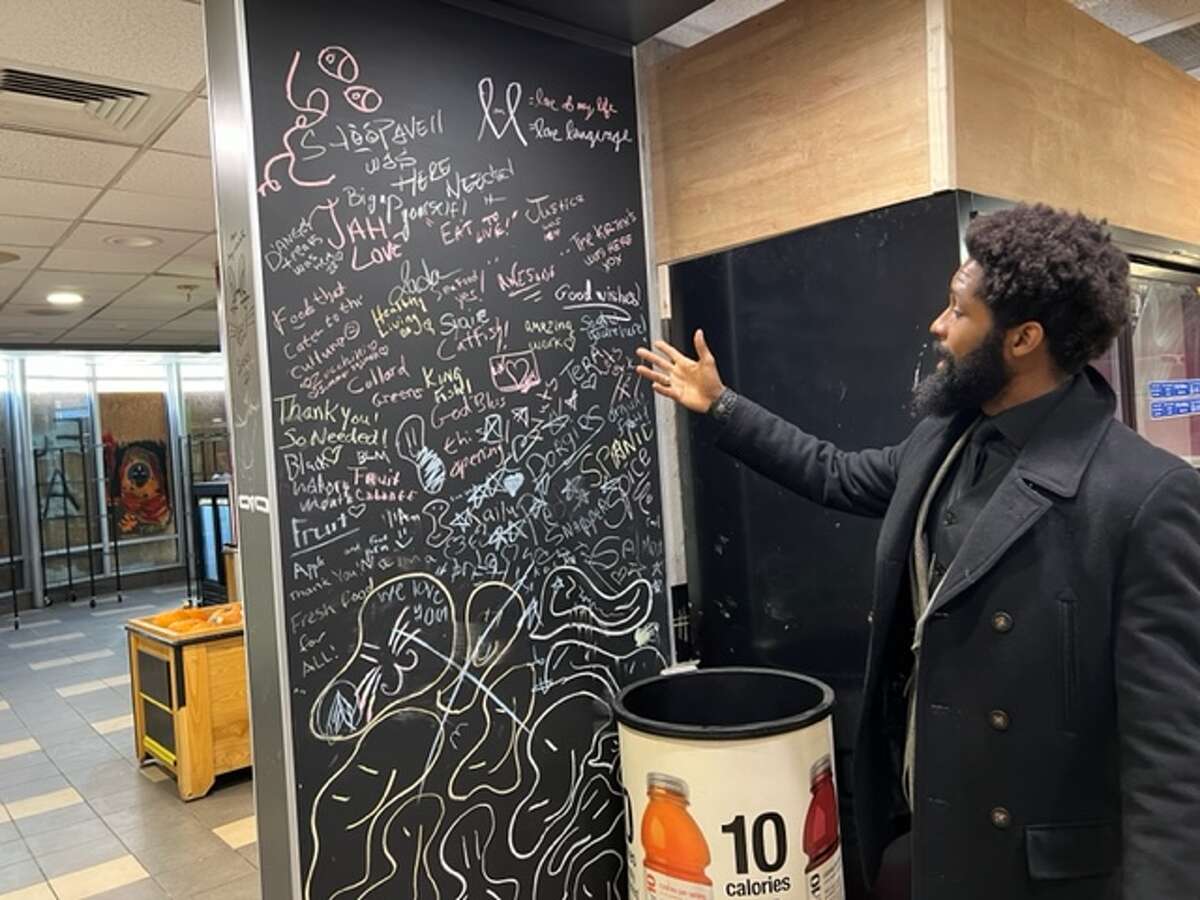 Travon Jackson points to a large blackboard where customers can leave messages, make suggestions and create artwork. 