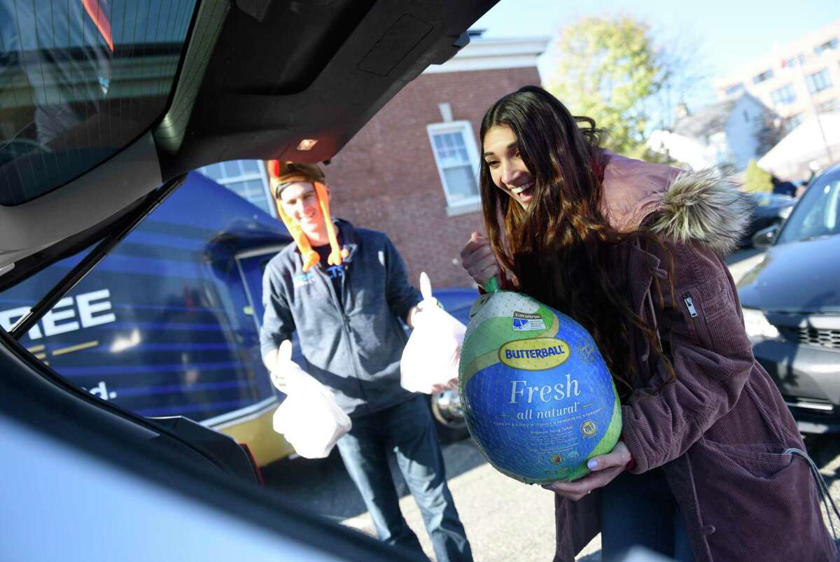 Chelsea Clark, a volunteer with the Sacred Heart University physician assistant program, loads a turkey into a car during the Person to Person turkey distribution at the East Norwalk Association Library in Norwalk, Conn. Tuesday, Nov. 22, 2022. The Person to Person distributed a total of 1,200 full Thanksgiving dinners, each including a turkey or chicken and several side dishes, between the three locations in Stamford, Darien, and Norwalk.
