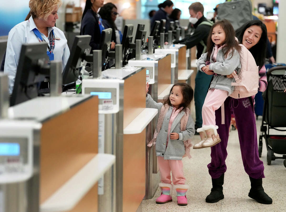 Hali Sims of Houston holds up her four-old-daughter, Jolie Sims, to see over the counter as she and her twin sister, Harlie Sims, watch and wave to the familyâs luggage as it moves along the conveyor belt behind the American Airlines ticket counter in Terminal A at George Bush Intercontinental Airport Tuesday, Nov. 22, 2022, in Houston. The family is going to Philadelphia for Thanksgiving.
