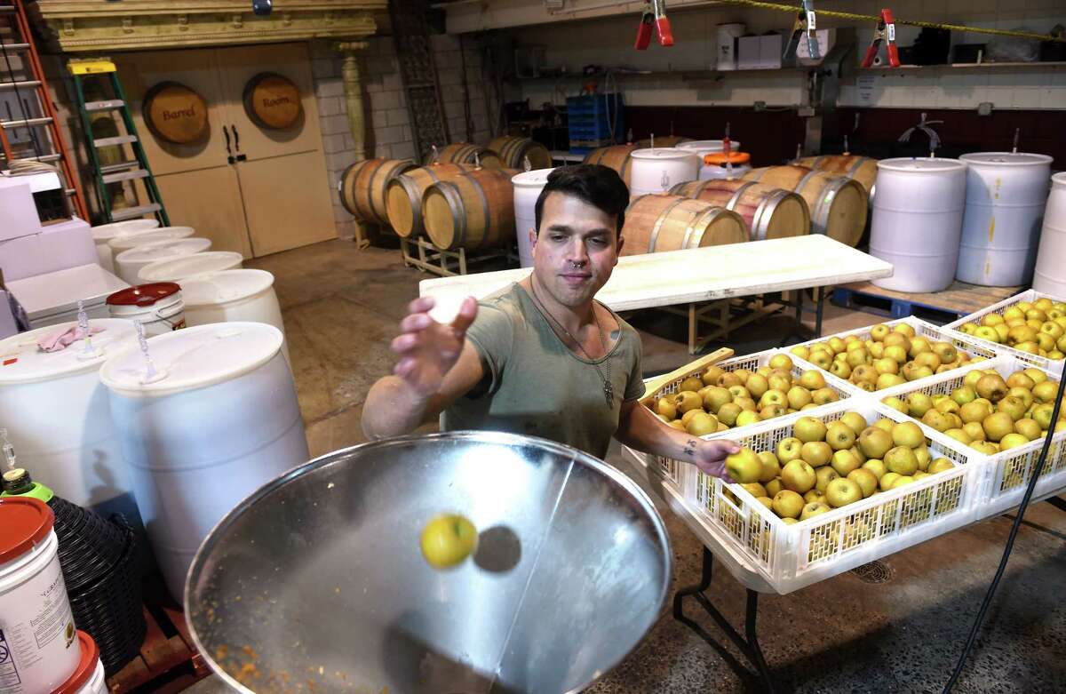 Ray Iannucci, owner of Valor Wines and Apple Theory, tosses Golden Russet apples into an apple crusher to yield apple mash at his microwinery in North Haven.