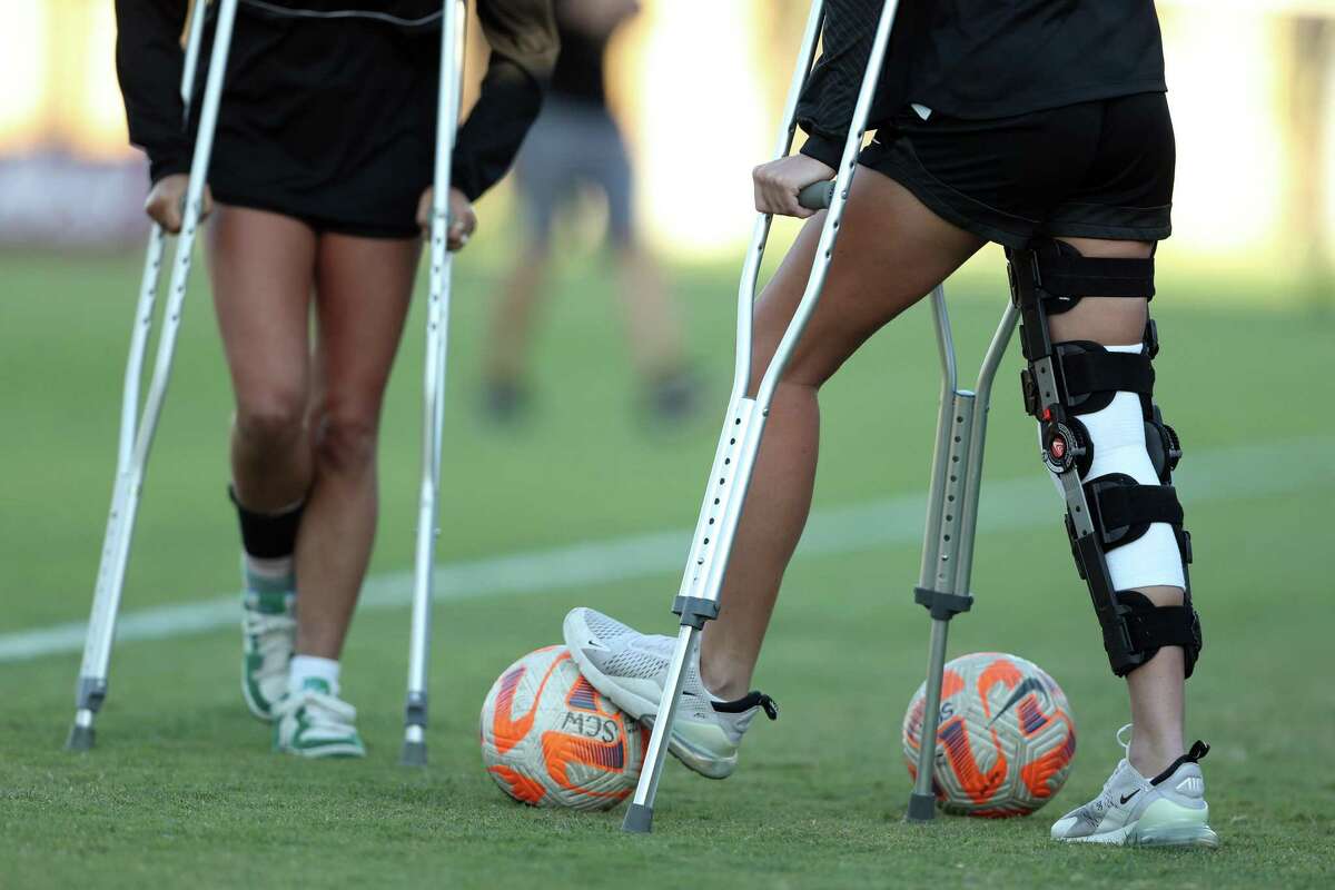 Santa Clara's Sally Menti (right), recovering from an ACL injury, stands on the sidelines with teammate Lucy Mitchell, who is recovering from an ankle injury.