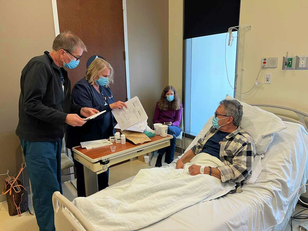 Rich Brotherton (left), nurse manager at the Stanford Clinical & Translational Research Unit, and Robin Howard, research nurse at Stanford Medicine, work with William Fimbres of Mountain View as his wife, Verna Fimbres, looks on. William Fimbres is participating in the nation's first clinical trial to see if the antiviral drug Paxlovid can treat the persistent symptoms of long COVID.