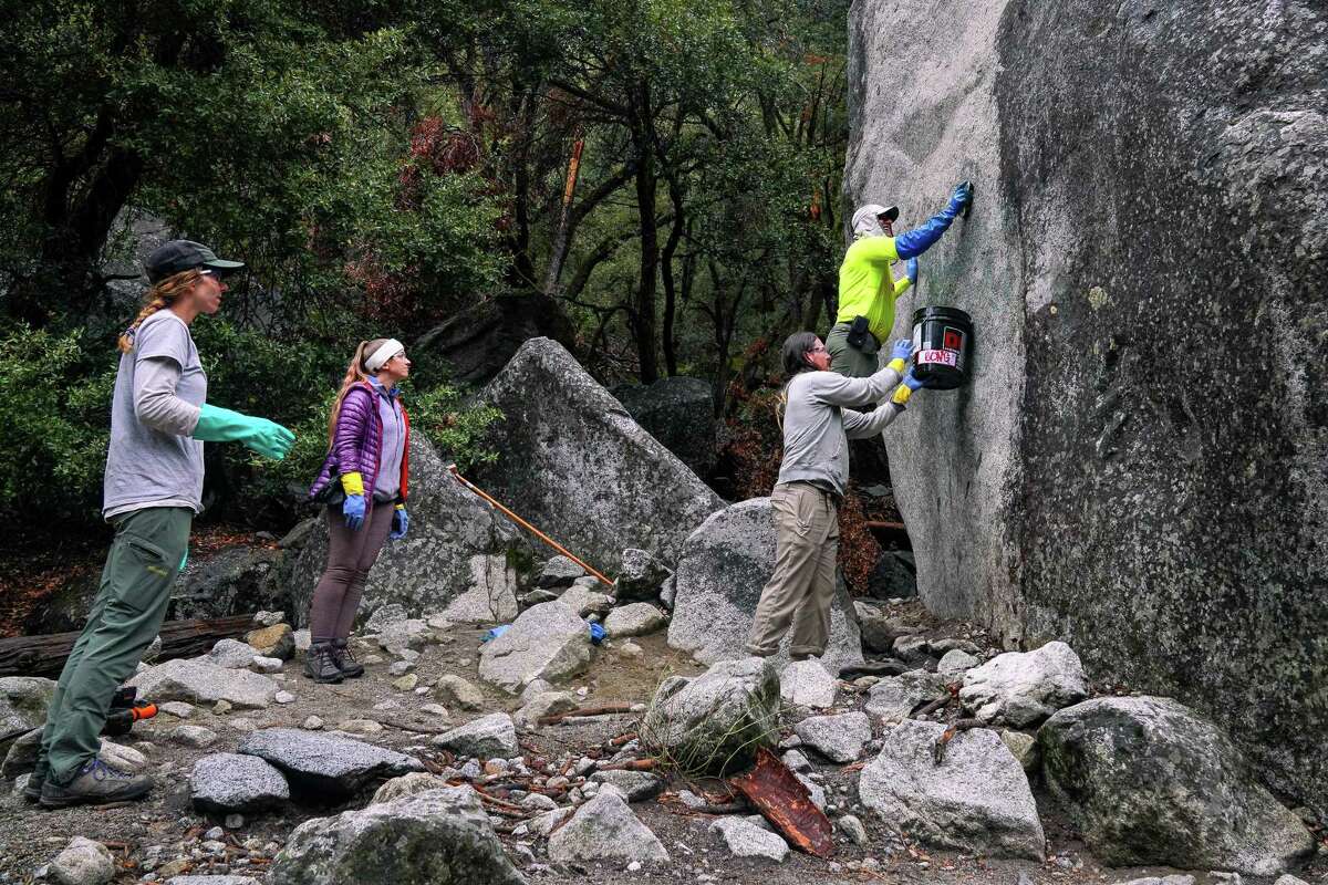 A Yosemite park ranger and volunteers try to remove graffiti on a boulder along the Yosemite Falls trail during this year’s Facelift event.