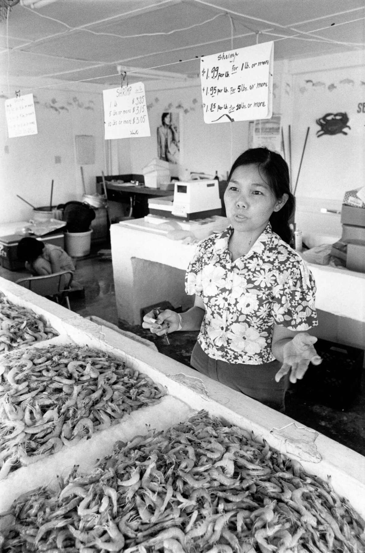 Tam Nguyen, 35, photographed in August of 1979 explains from behind the counter of her brother's fish house in Seabrook that her people feel welcome at their new home on Galveston Bay but don't understand many of the laws and customs.
