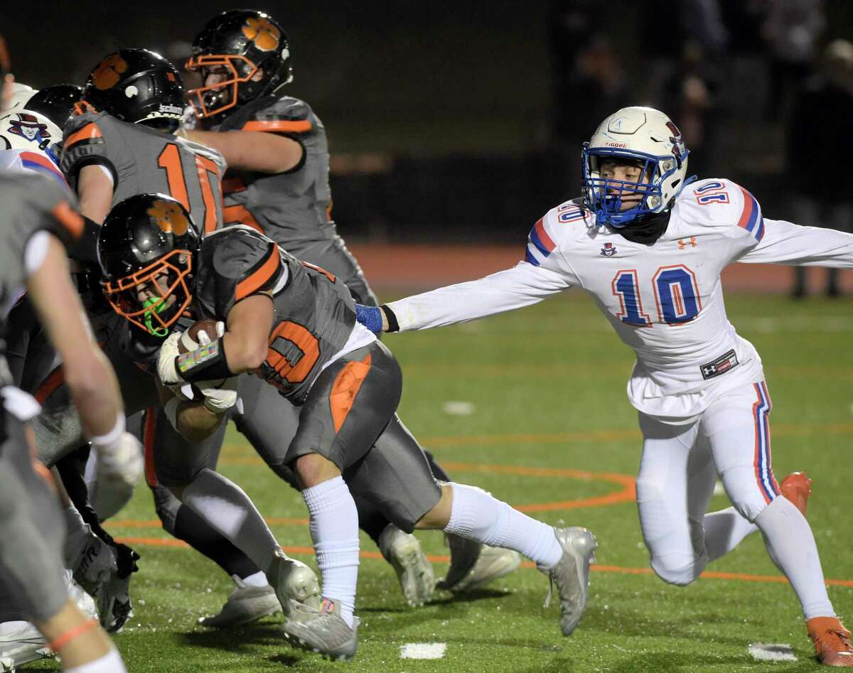 Danbury’s Roman Zelenstsky (#10) tries to grab Ridgefield’s Kai Kywata (#20) as he hits the line in the first half of the high school football game between Danbury and Ridgefield high schools, Wednesday night, November 23, 2022, at Ridgefield High School, Ridgefield, Conn. Kywata scored a touchdown on the play.