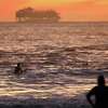 在加利福尼亚州索萨利托的罗迪欧海滩，一名冲浪者和一名海滩爱好者看着一艘游轮驶向大海，