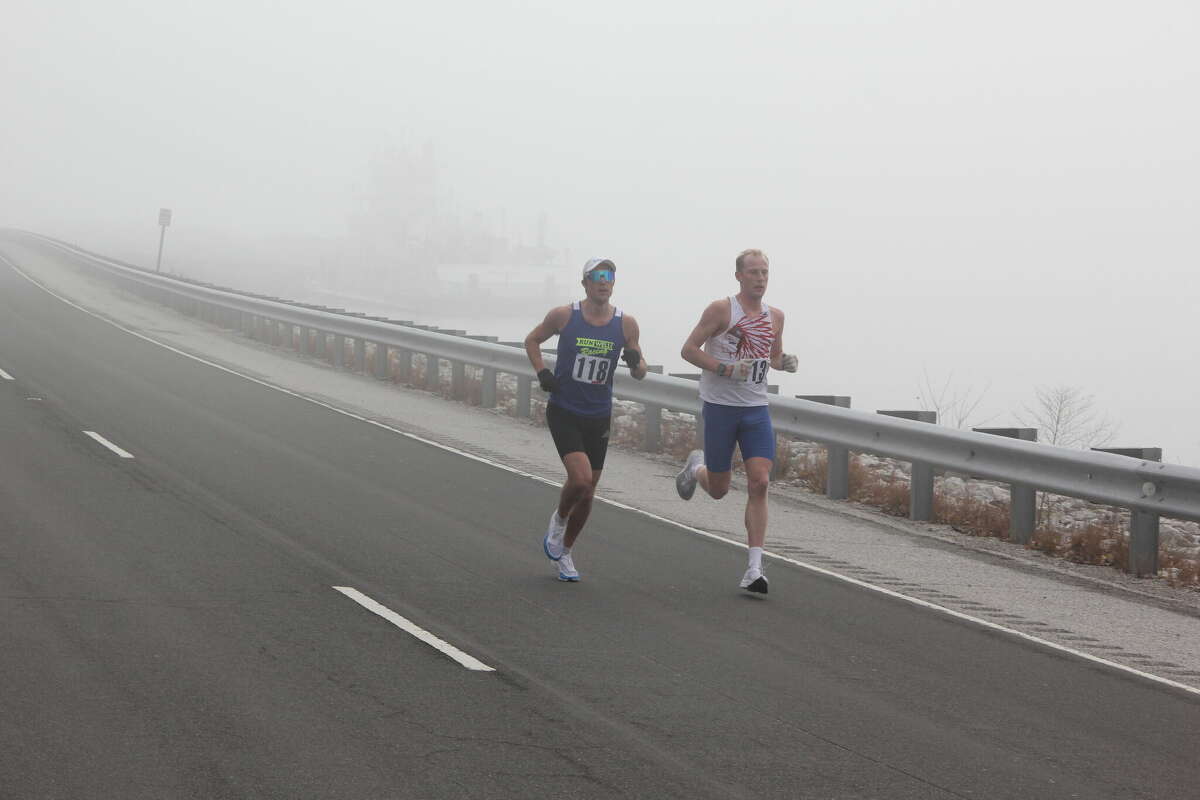 Luke Padesky (118), left, of St. Louis, and William O’Keefe (113), of Granite City, lead the pack during Saturday’s Great River Road Run, a 10-mile run sponsored by the Alton Road Runner’s Club. The scenery that makes up much of the charm of the race was largely obscured by heavy fog. Behind Padesky and O’Keefe, a tugboat and barges tied up along the bank are obscured by the fog. About 360 people participated this year.