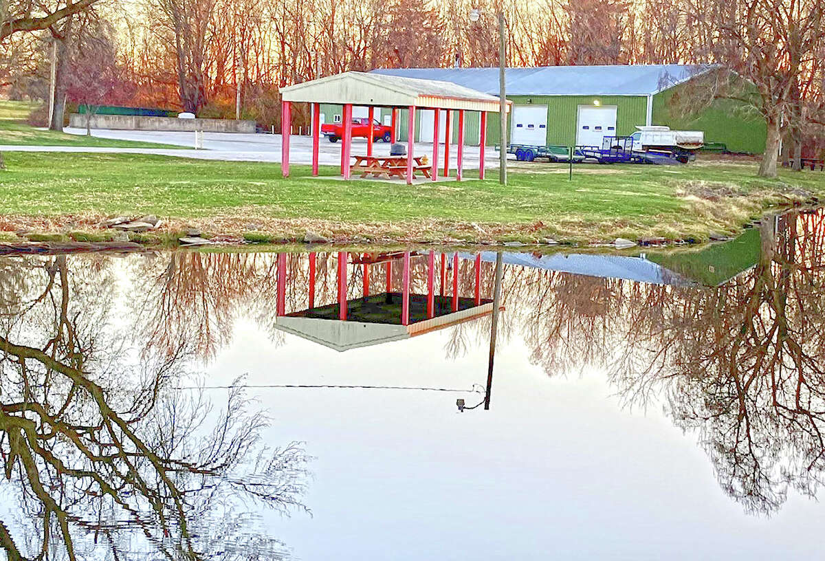 A picnic shelter and bare trees are reflected in the water of a lake at Nichols Park.