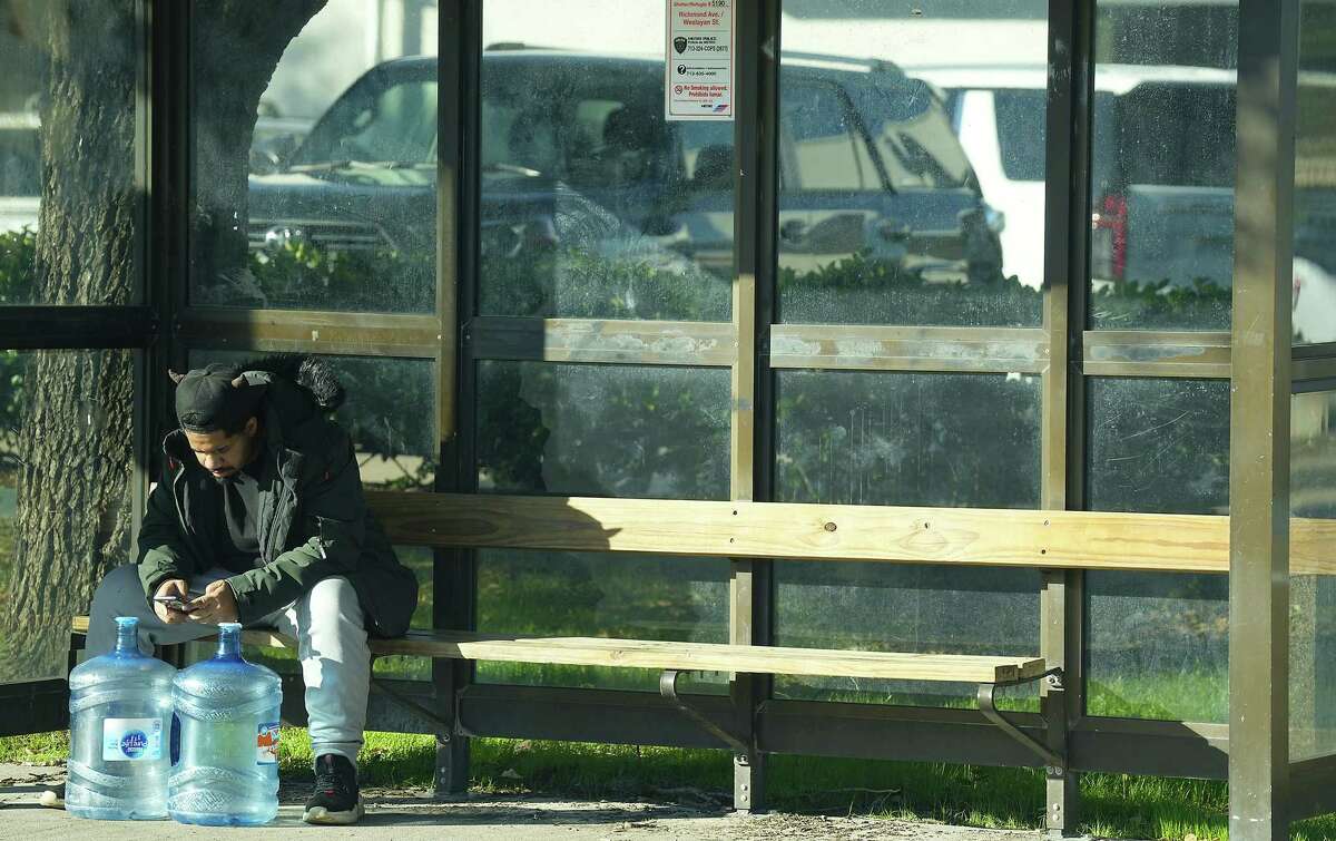 A man waits at a bus stop on Richmond Ave., with two empty 5-gallon water bottles on Monday, Nov. 28, 2022 in Houston.