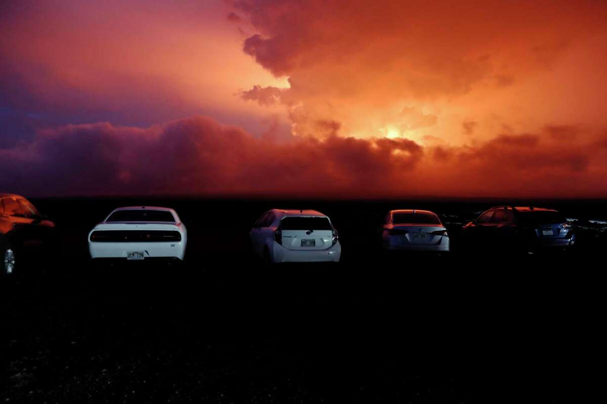 Cars are parked near an ancient lava field as a lava flow colors the sky above Mauna Loa, Monday, Nov. 28, 2022, near Hilo, Hawaii. Mauna Loa, the world's largest active volcano, erupted Monday for the first time in 38 years.