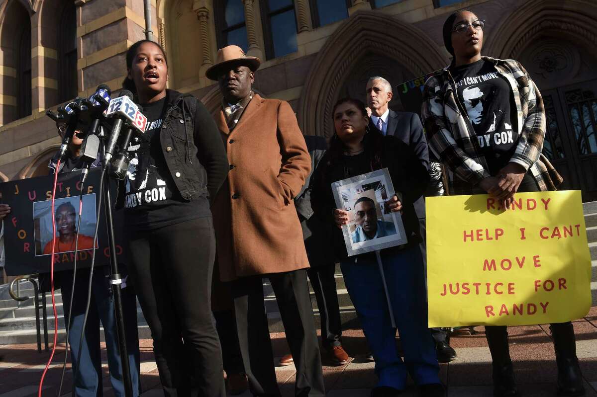 Attorney Benjamin Crump, center, listens to LaToya Boomer, left, sister of Richard "Randy" Cox, speak at a news conference in front of City Hall in New Haven on November 29, 2022 following the arrest of five New Haven Police officers in connection with injuries sustained by Cox while in police custody. At far right is Cox's sister, LaQuavius LeGrant.