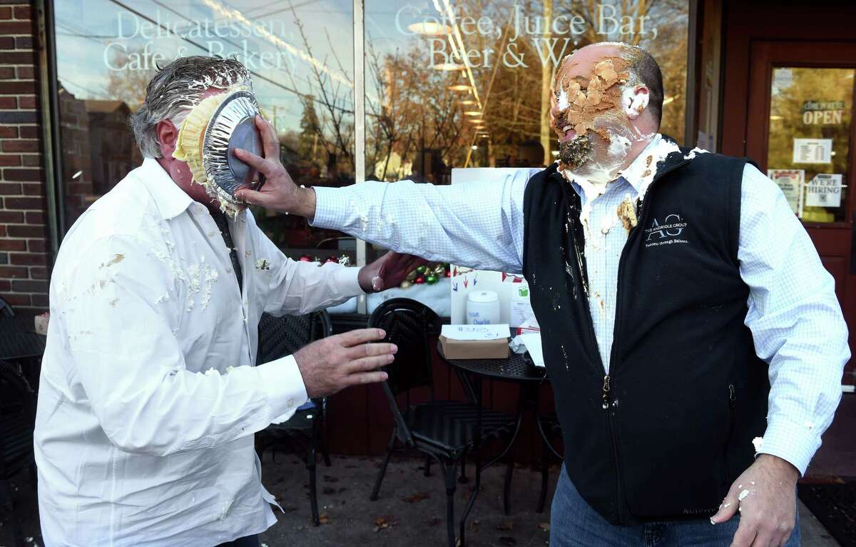 Charlie Andriole, left gets a banana cream pie in the face from Rob DeLucca, who has the remains of a pumpkin pie topped with whipped cream on his face, in front of The Marketplace at Guilford Food Center on November 29, 2022 as part of the Pie Wars Challenge on Giving Tuesday. Funds raised benefit the Community Dining Room.