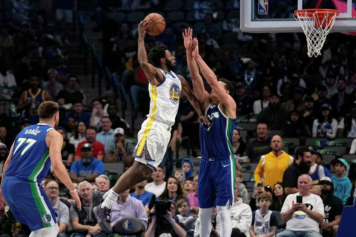 Golden State Warriors forward Andrew Wiggins goes up to attempt a dunk between Dallas Mavericks' Luka Doncic and Dwight Powell, right, in the first half of an NBA basketball game in Dallas, Tuesday, Nov. 29, 2022. (AP Photo/Tony Gutierrez)