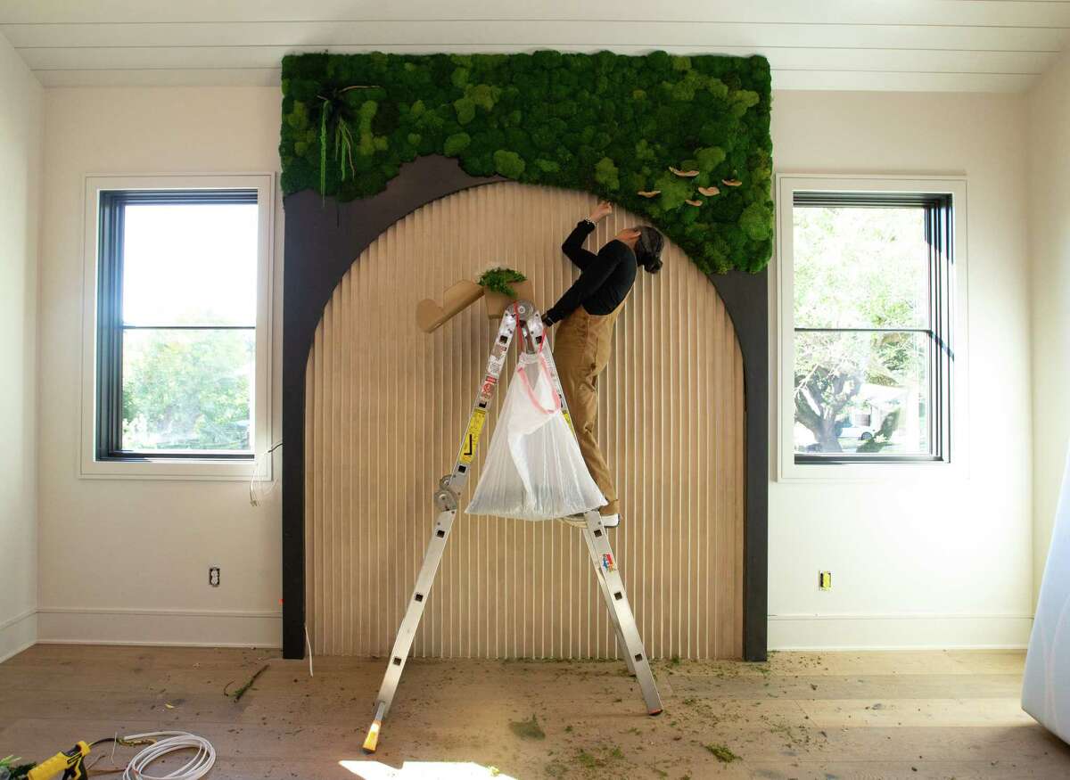 Priscilla Saynay of Ms. Moss Potter applies preserved moss and other plants on an accent wall in the primary bedroom.