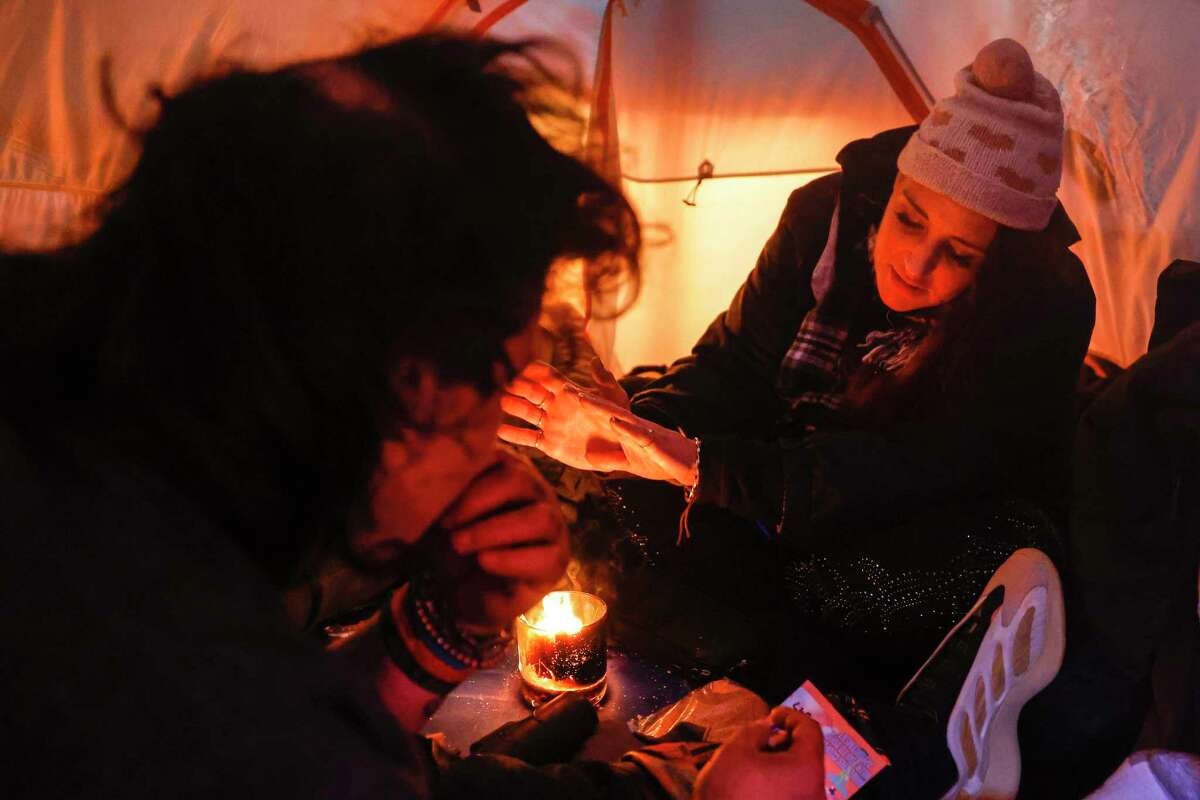 Rico Mallida and Aly May warm themselves around a small fire made from wax and hand sanitizer as they sleep in a tent in the rain along Myrtle Street in San Francisco.