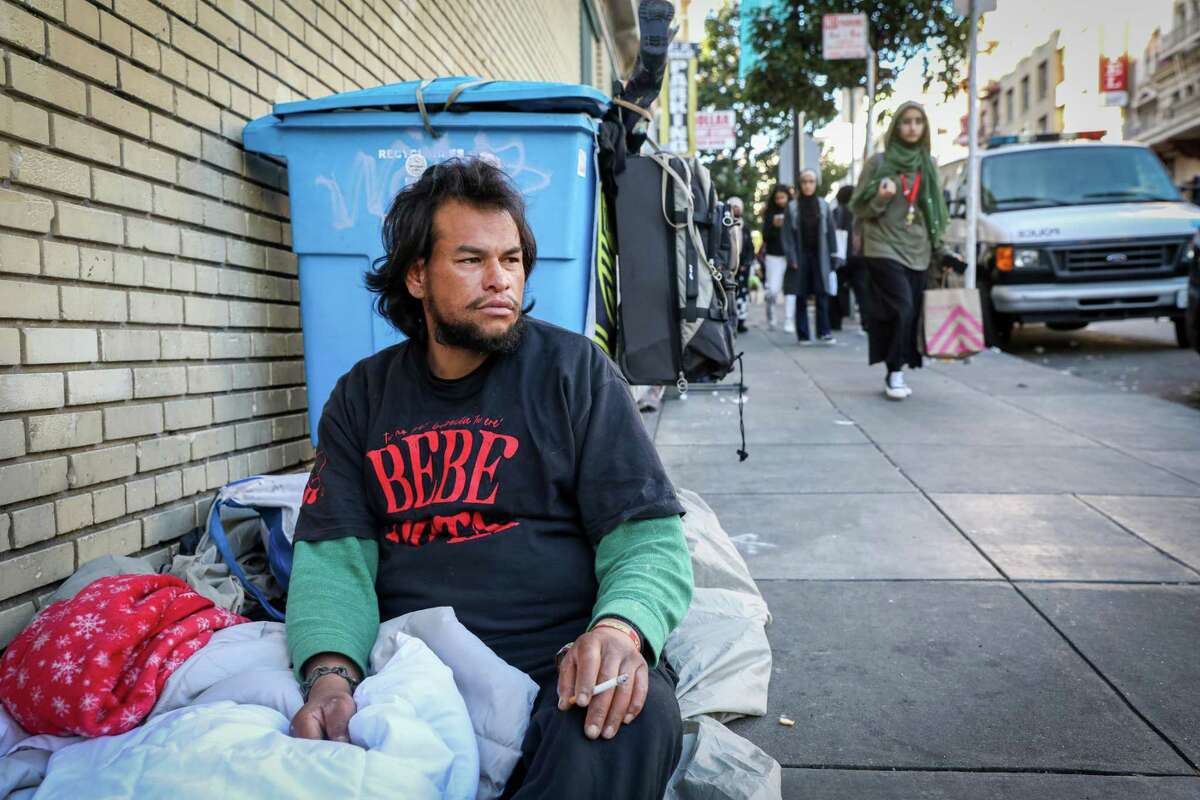 Jason Gallindo, 28, sits near his belongings at the intersection of Jones and Eddy streets in the Tenderloin. As a cold front and rain drench the Bay Area this week, Gallindo said he stays warm with a comforter and fleece blanket. Gallindo said he has been living on the streets in San Francisco for a year and prefers it over shelters.