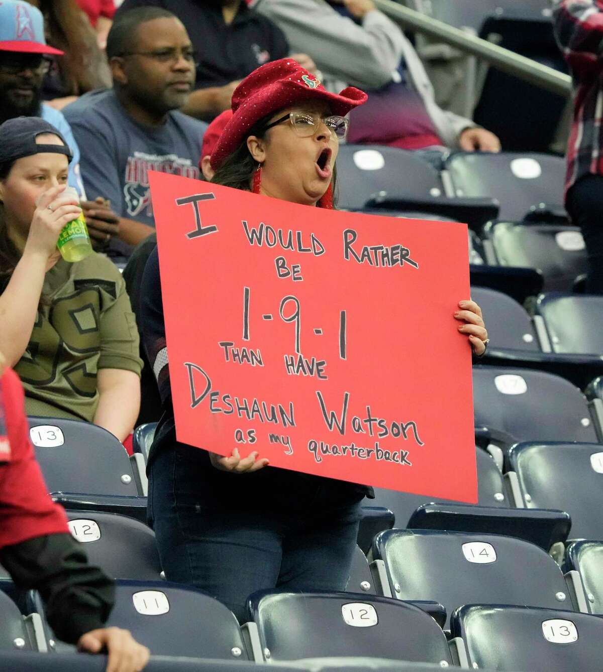A woman holds a sign protesting Cleveland Browns quarterback Deshaun Watson during the first quarter of an NFL football game at NRG Stadium on Sunday, Dec. 4, 2022 inHouston .